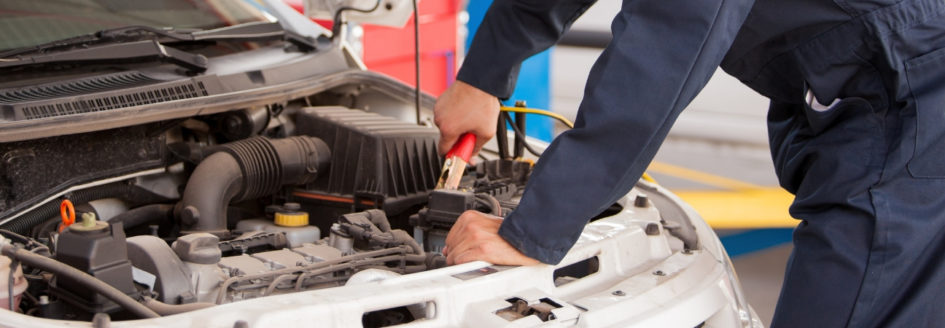 Auto mechanic hooking up a jumper cable to a car battery